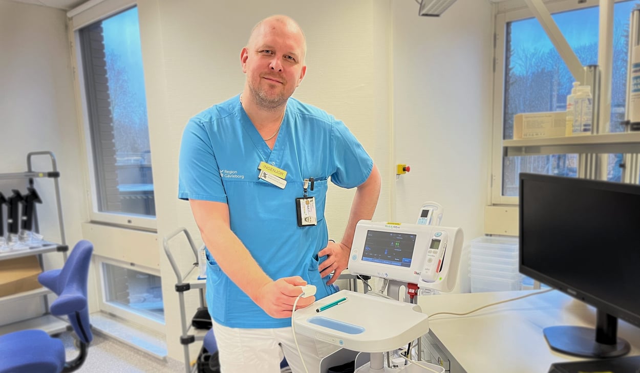 Rickard  Nilsson står i vårdkläder intill monitor.